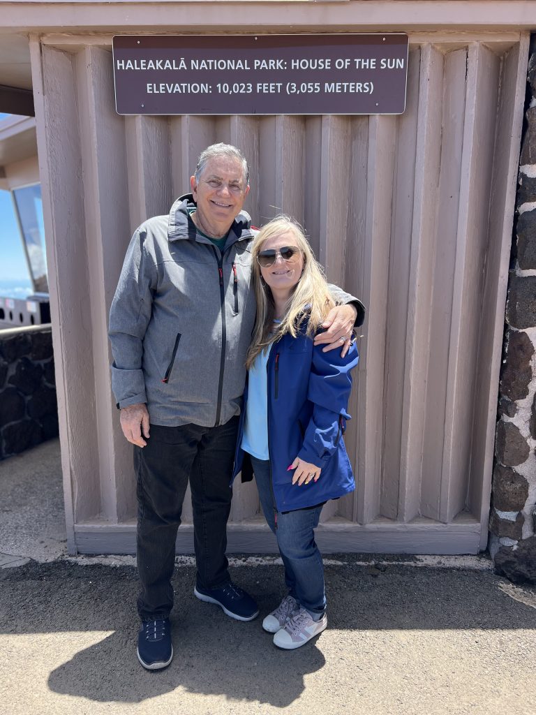 We are standing front of sign that reads "Haleakala National Park: House of the Sun. Elevation: 10,023 feet (3,055 meters)